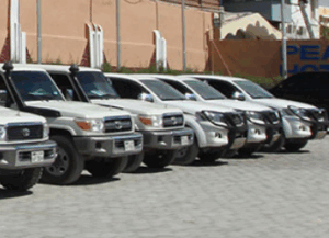 Somalia Airport Secure Escort and Immigration Assistance A row of white SUVs, likely Toyota Land Cruisers, are parked on a paved lot in front of a building with "PEACE HOTEL" partially visible.