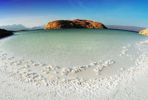 A serene landscape of a salt lake with an island in the distance, under a clear blue sky.
