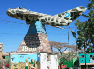 Sheikh Mountains Roadtrip and Hike and Hargeisa City Tour A monument featuring a camouflaged warplane atop a pyramid-shaped base with inscriptions and murals stands against a clear blue sky.